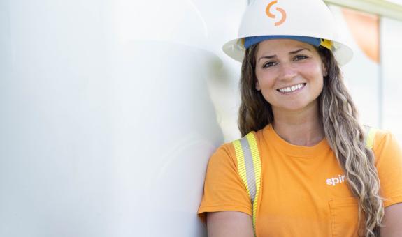 Image of Spire employee in her uniform and hard hat. She is leaning against a work van.