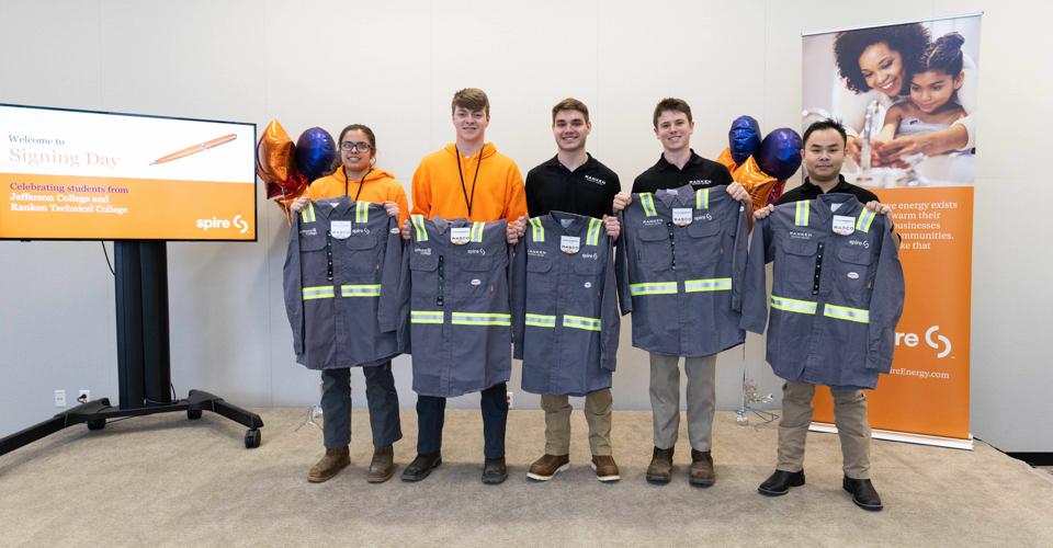 Image of Spire co-op students standing indoors and holding up grey work uniforms