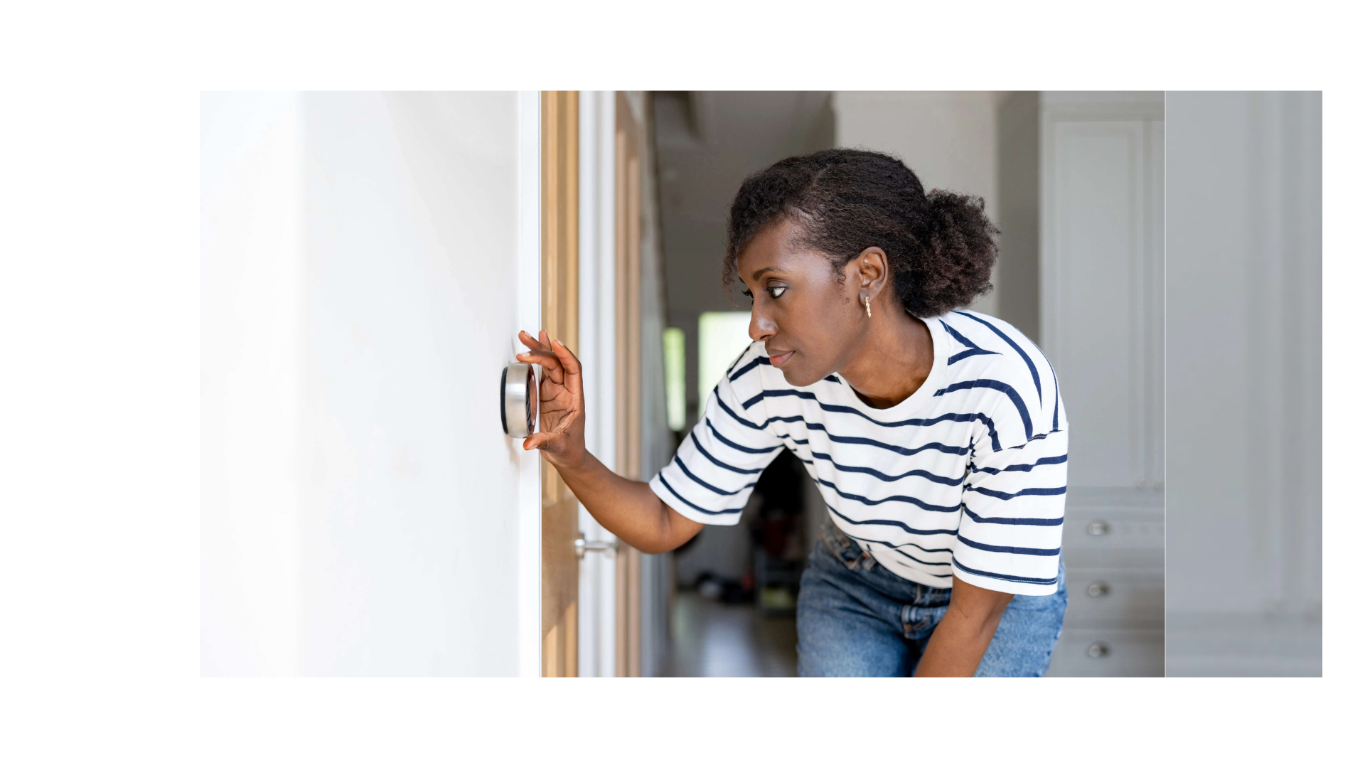 Image of African American woman adjusting her smart thermostat inside her home